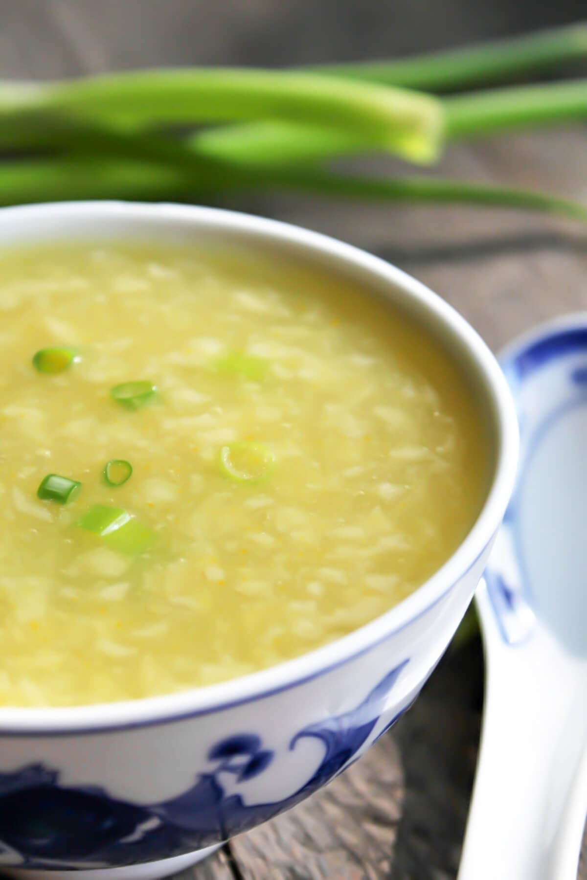 Vegan egg drop soup in a white bowl with green onions behind it.