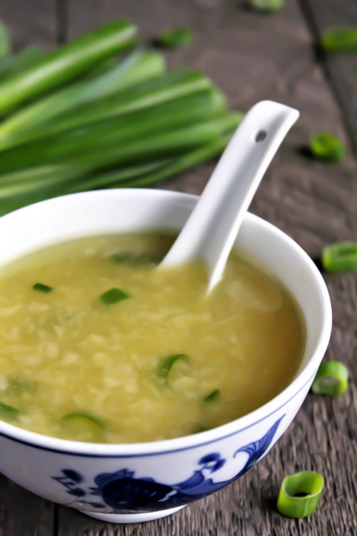 Vegan egg drop soup in a white bowl with green onions behind it.