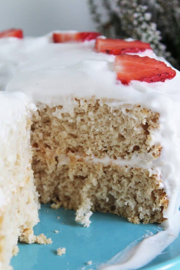 A vegan angel food cake with a slice cut out of it topped with vegan whipped cream and strawberries.