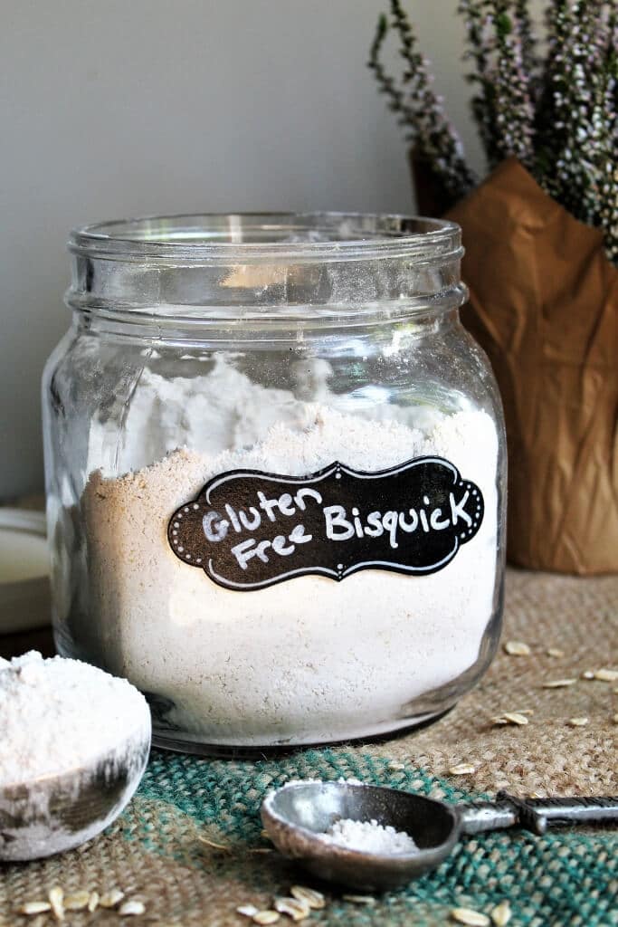 A glass container filled with gluten-free Bisquick with measuring cup in front of it.
