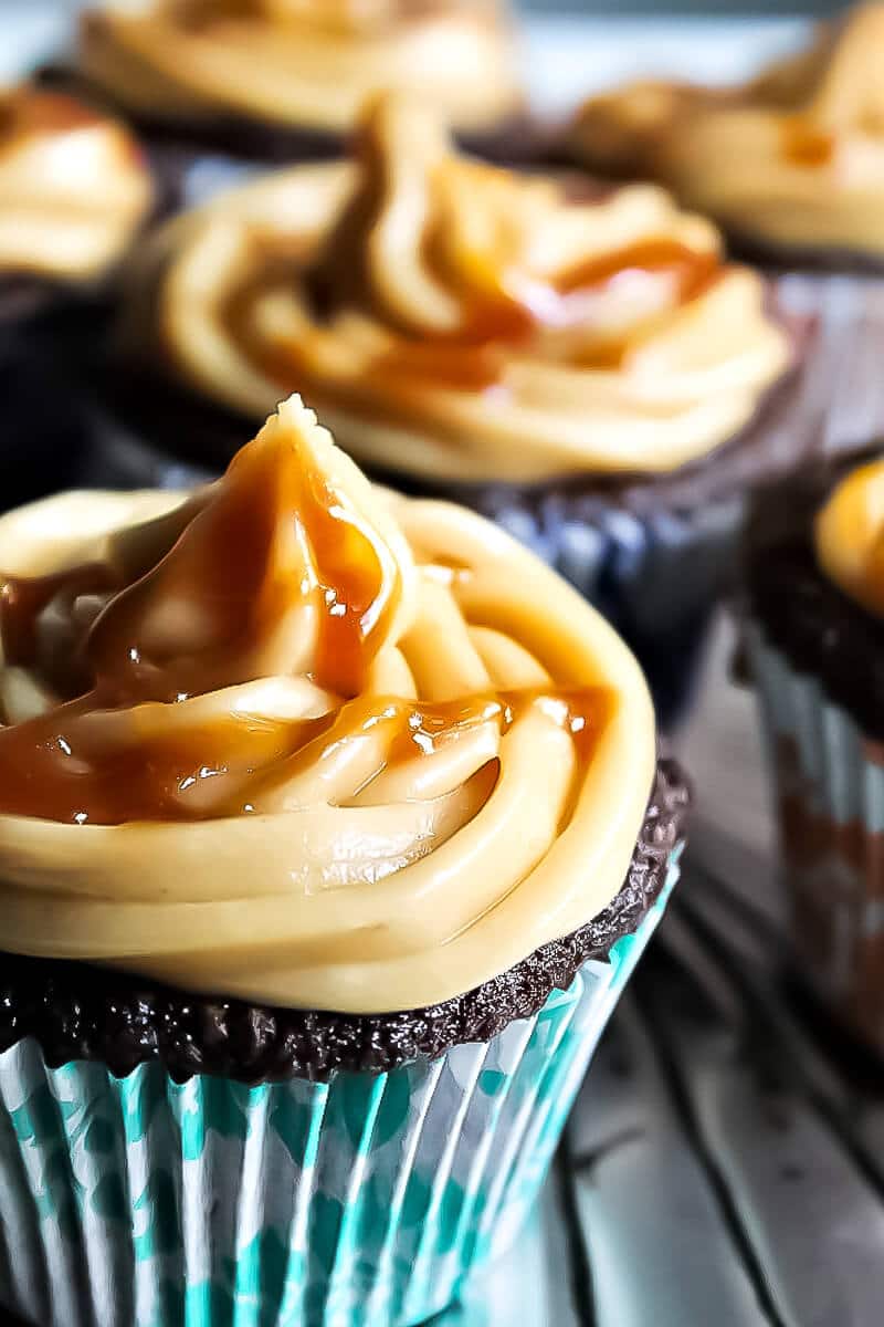 A vegan chocolate cupcake with caramel frosting with caramel drizzle with more behind it.