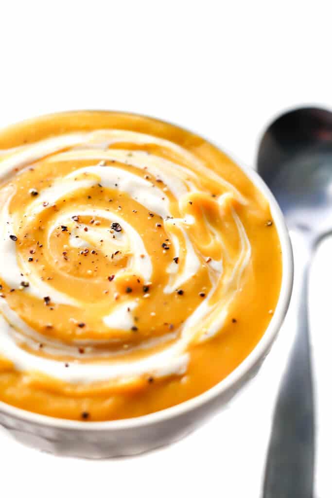 A close up of a bowl of vegan squash soup with a spoon on the side. 