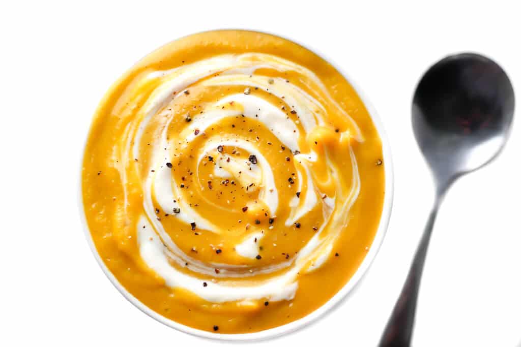 An overhead shot of a bowl of vegan butternut squash soup with vegan sour cream swirled into it.