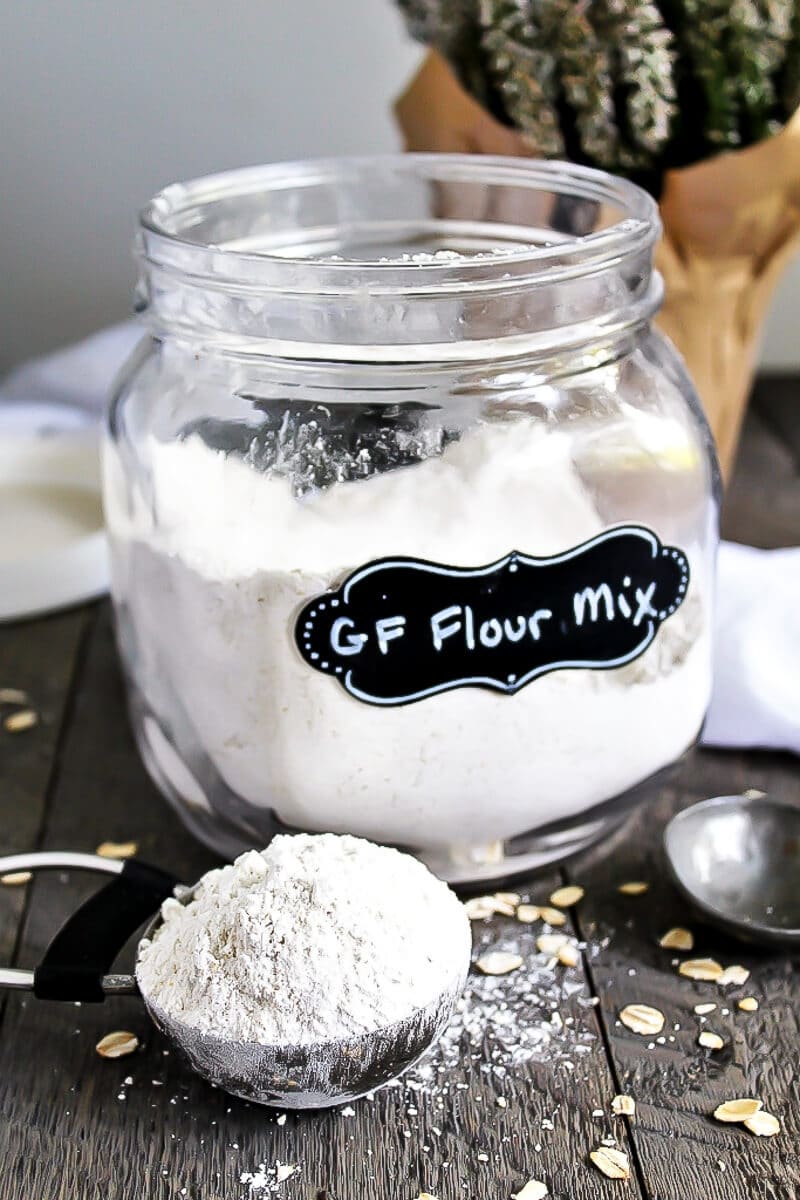 A glass jar filled with vegan gluten-free flour mix with a cup of flour in front of it. 