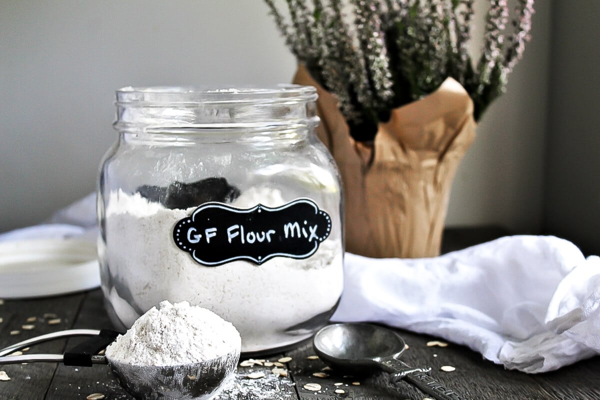 A homemade gluten-free flour mix in a glass jar with a scoop taken out.