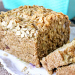 A loaf of vegan beer bread with oats on top sliced on a plate.