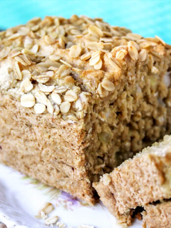 A loaf of vegan beer bread with oats on top sliced on a plate.