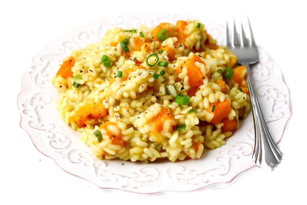 A white plate full of creamy vegan butternut squash risotto topped with slices of green onion,