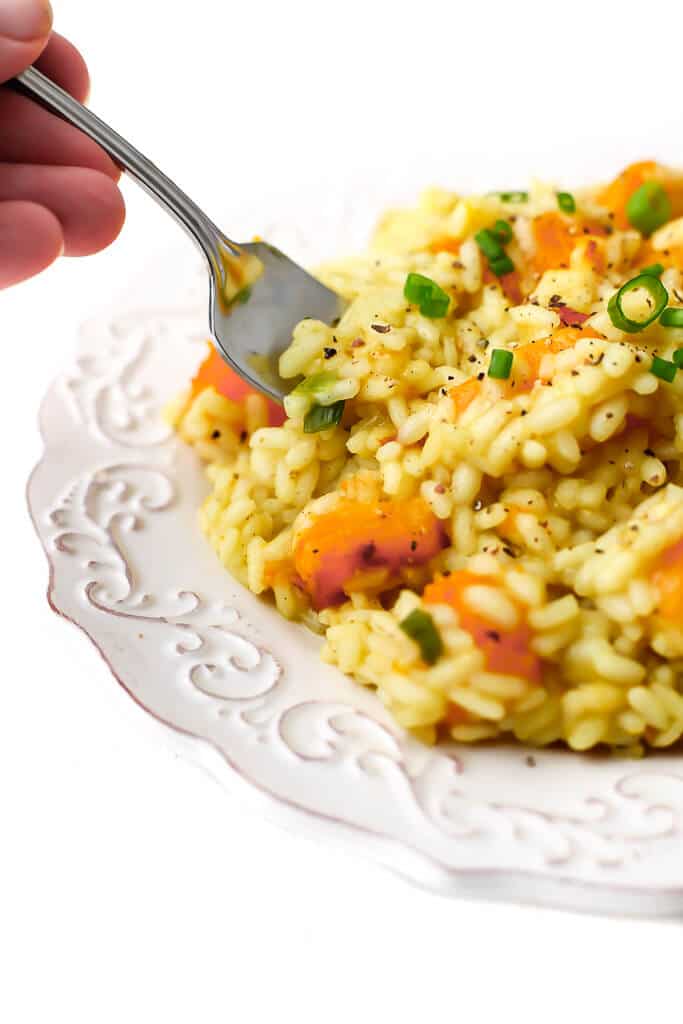 A plate of vegan butternut squash risotto with someone taking a fork full.