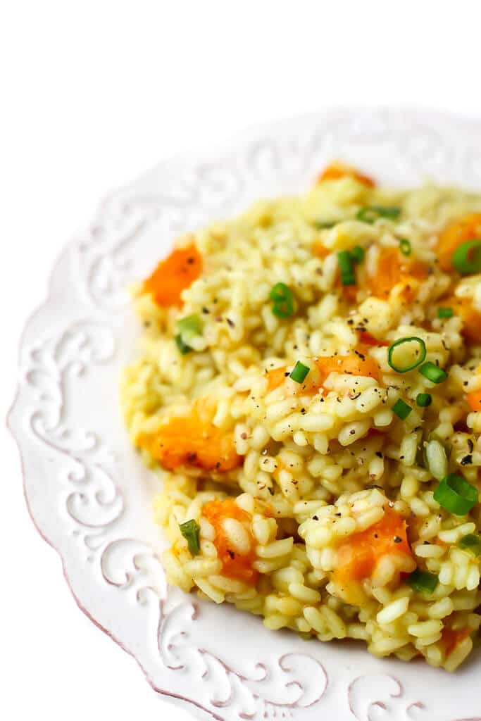 A white plate full of creamy vegan butternut squash risotto topped with slices of green onion and black pepper.