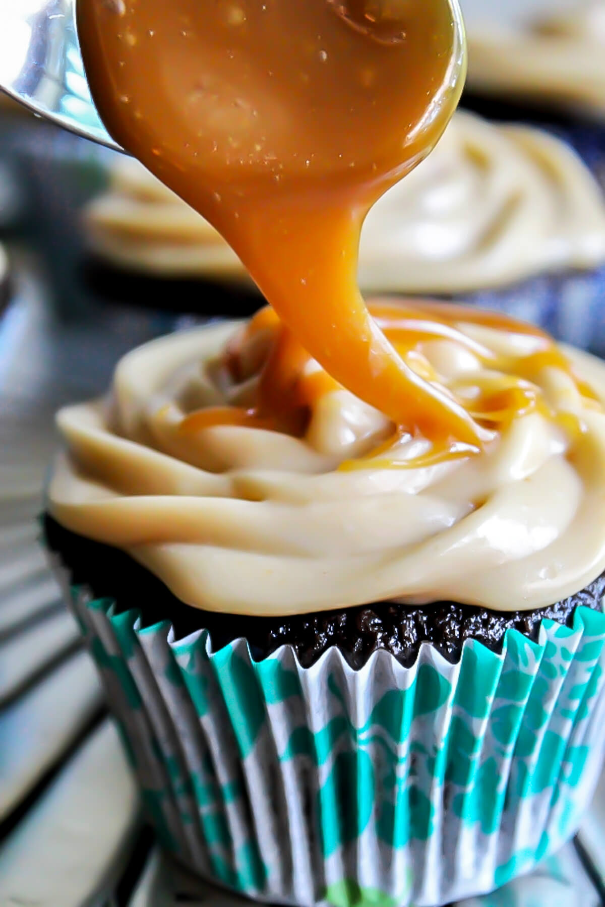 A chocolate cupcake in a blue wrapper with vegan caramel frosting and salted caramel sauce being drizzled over top of it.