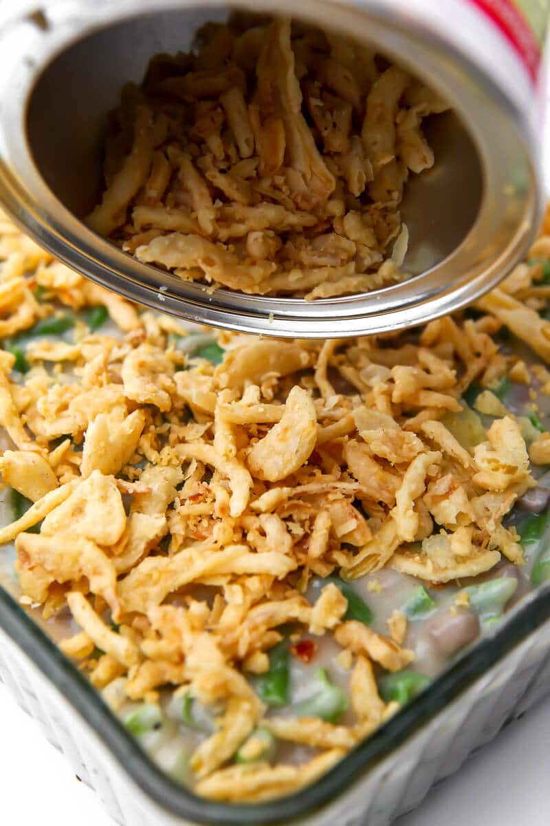 Green bean casserole being sprinkled with French fried onions on top.