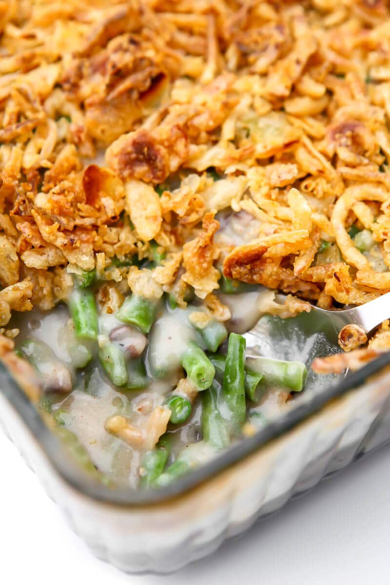 A close up of a vegan green bean casserole with French fried onions on top and a scoop taken out of it.