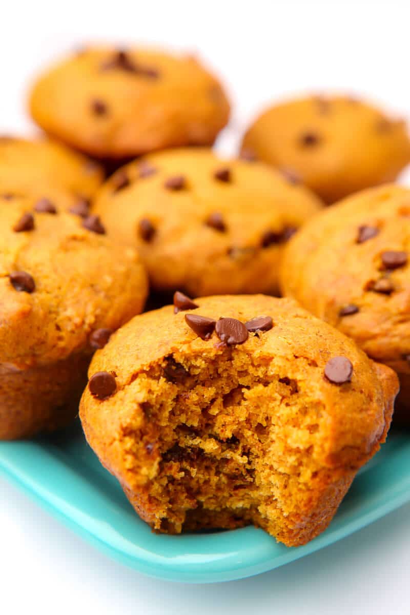 A turquoise plate filled with vegan pumpkin muffins with chocolate chips. One muffin has a bite taken out of it.