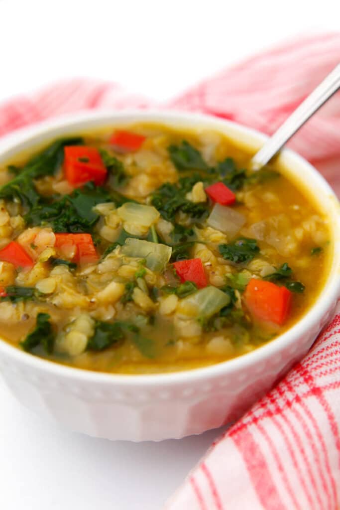 A bowl of red lentil soup with red peppers and kale in a pumpkin curry broth.