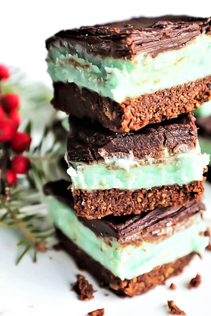 A stack of three vegan creme de menthe squares layered with chocolate graham cracker, mint filling and melted chocolate.
