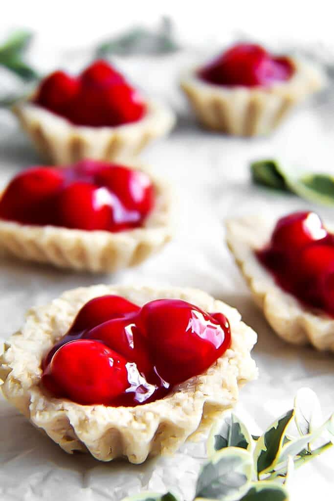 Vegan and gluten free Swedish tarts filled with cherry pie filling on a white tray.