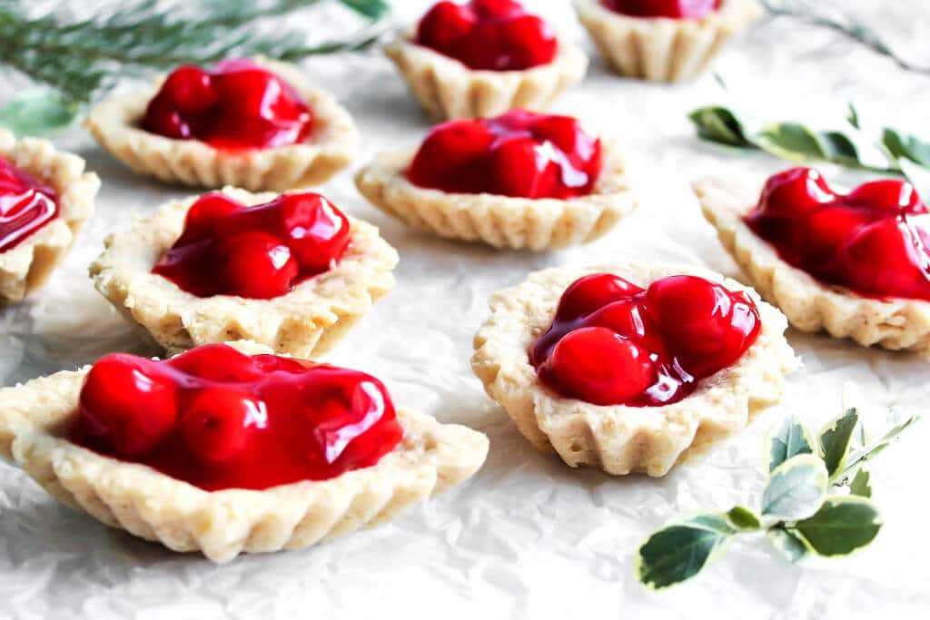 Swedish tarts also known as Sand Bakkels filled with red cherry pie filling with greens around them.
