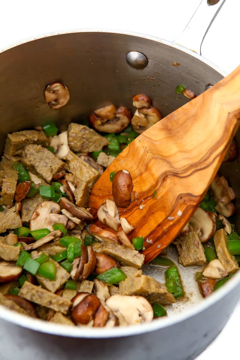 Mushrooms, green peppers, and vegan seitan chicken strips sautéing in a pan.