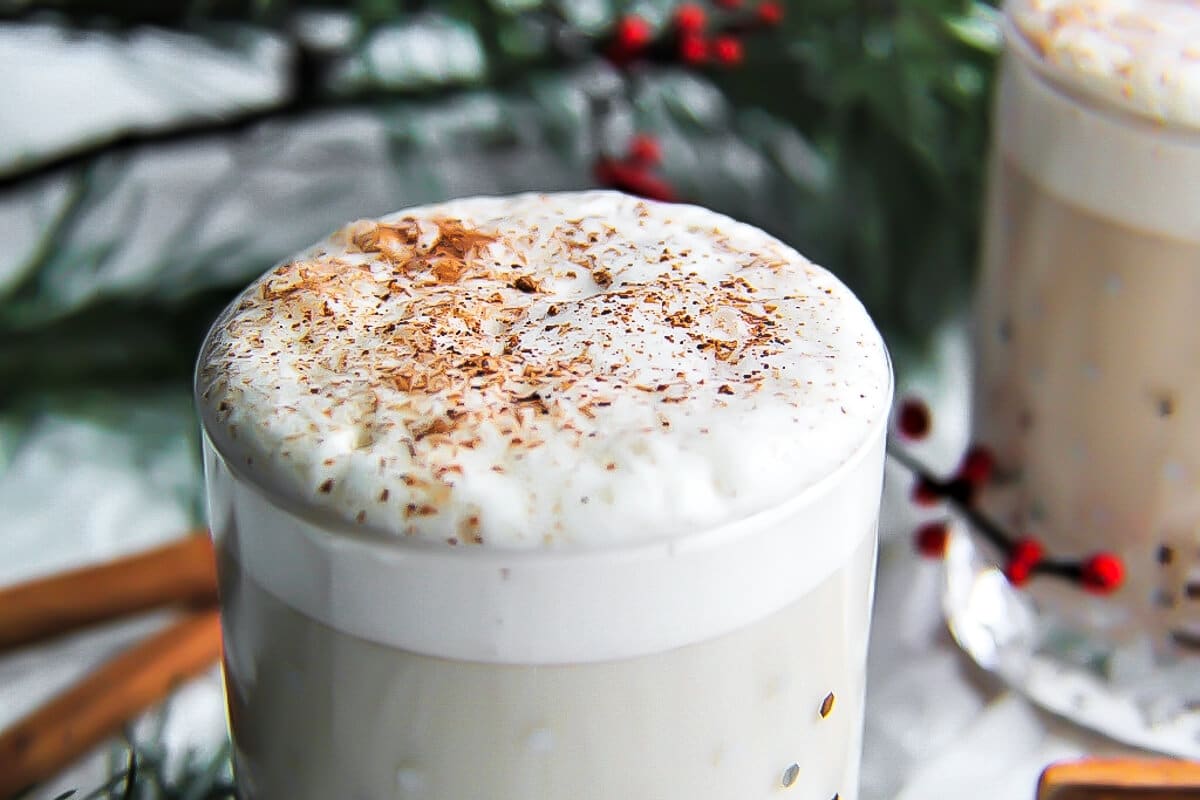 A white foamy head on a glass of homemade dairy-free eggnog sprinkled with nutmeg.