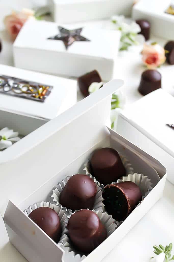 An open box of homemade dairy-free chocolates and more pretty white chocolate boxes behind it.