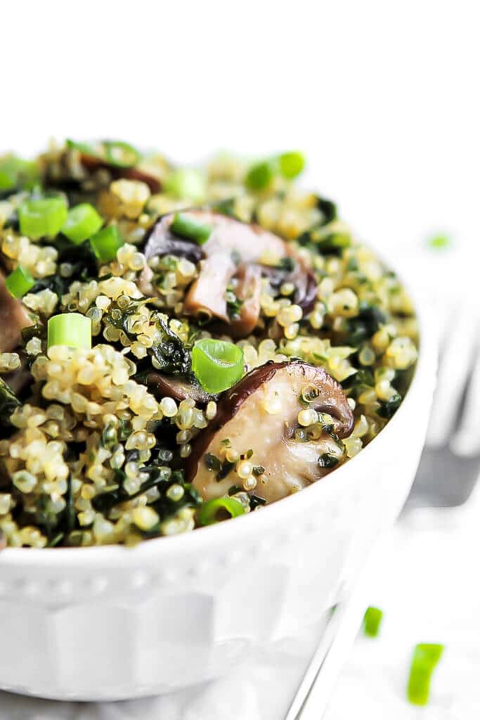A white bowl filled with sauteed mushrooms, quinoa and kale and topped with green onions.