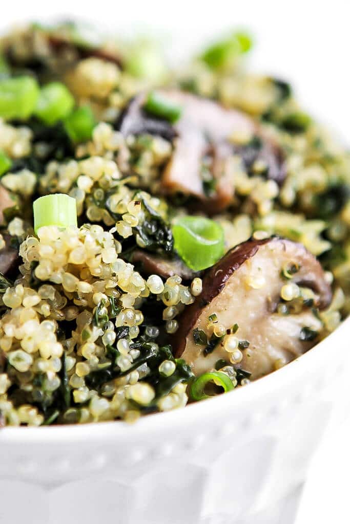 A bowl filled with quinoa and kale with sauteed mushrooms and topped with green onions.