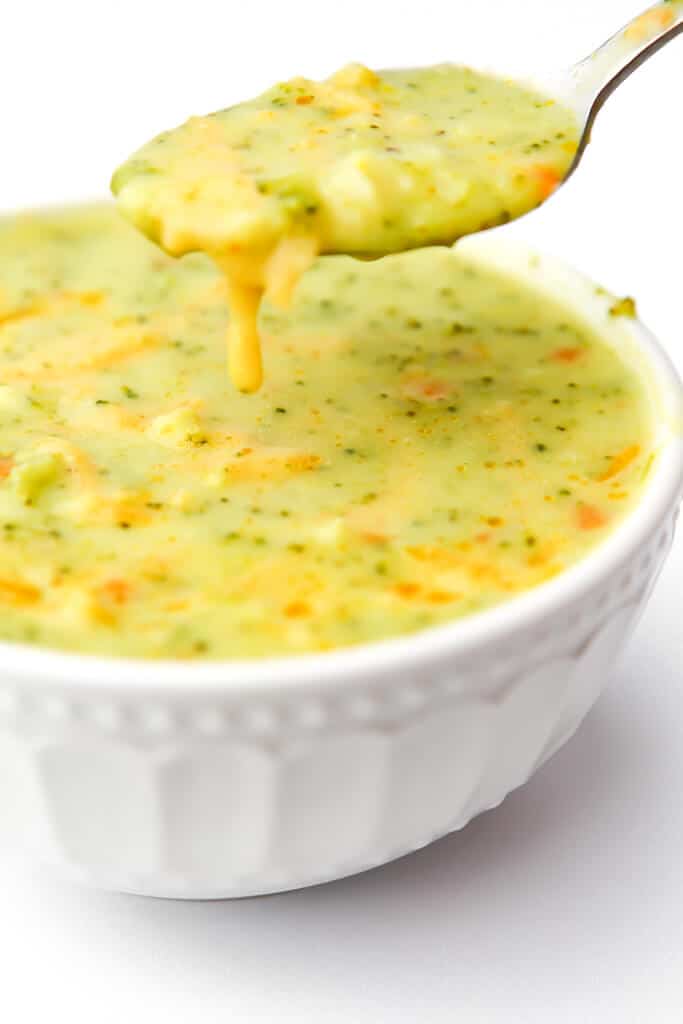A bowl of vegan broccoli cheese soup with a spoonful of soup above it.