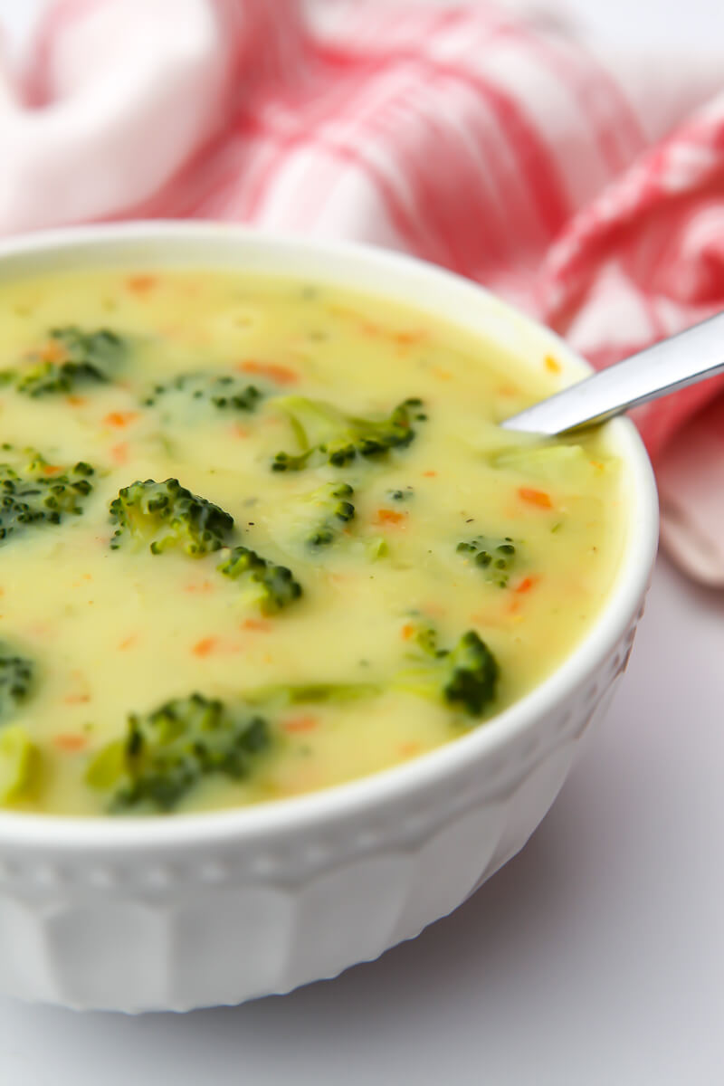 A bowl of gluten-free and dairy-free cream of broccoli soup with a red tea towel behind it and a spoon in the bowl.