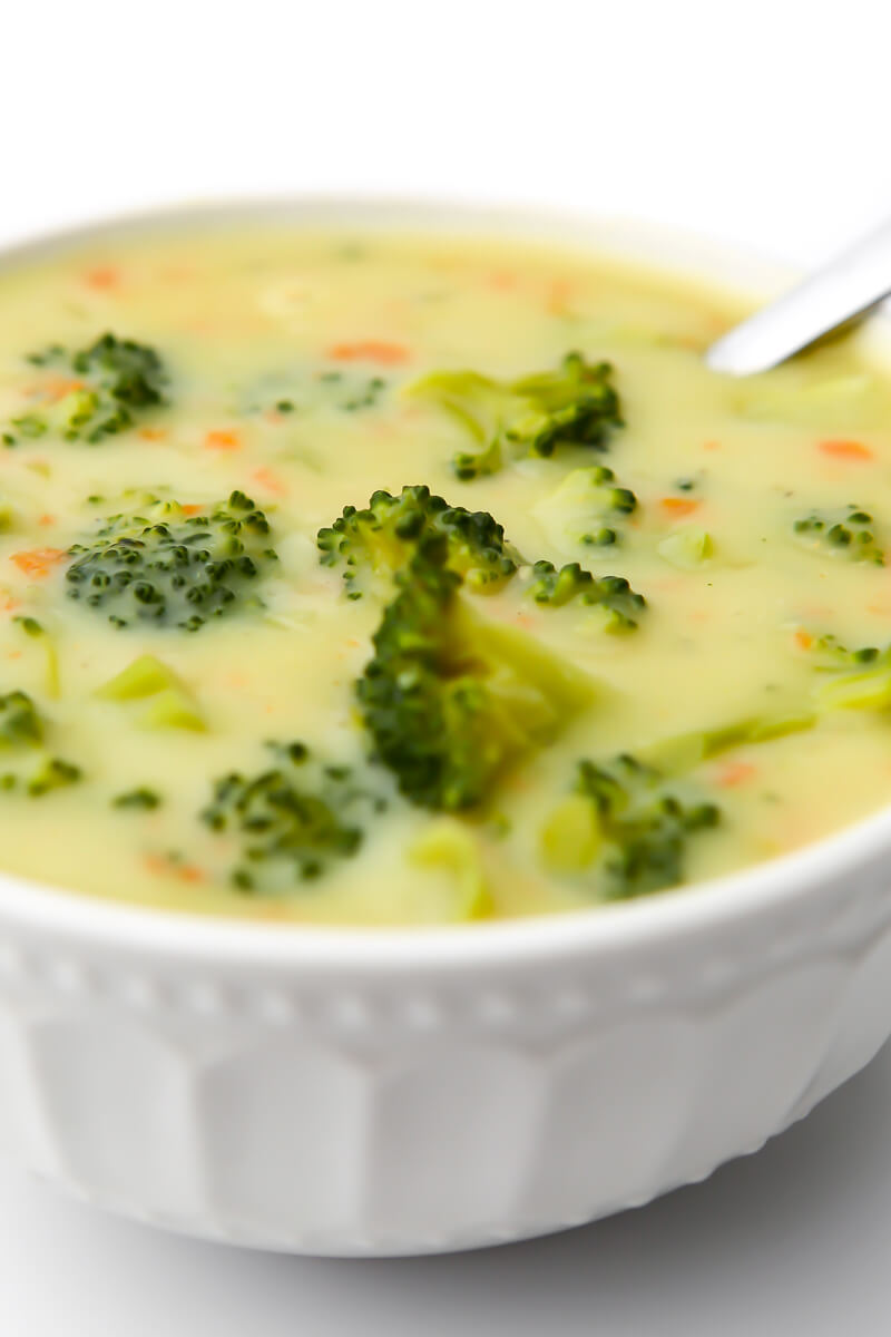 A white bowl filled with creamy vegan broccoli soup with a spoon in it.