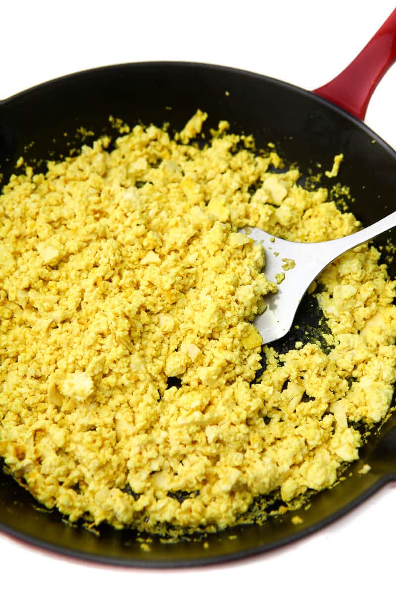 Vegan scrambled eggs cooked in an iron skillet with a spatula in it.