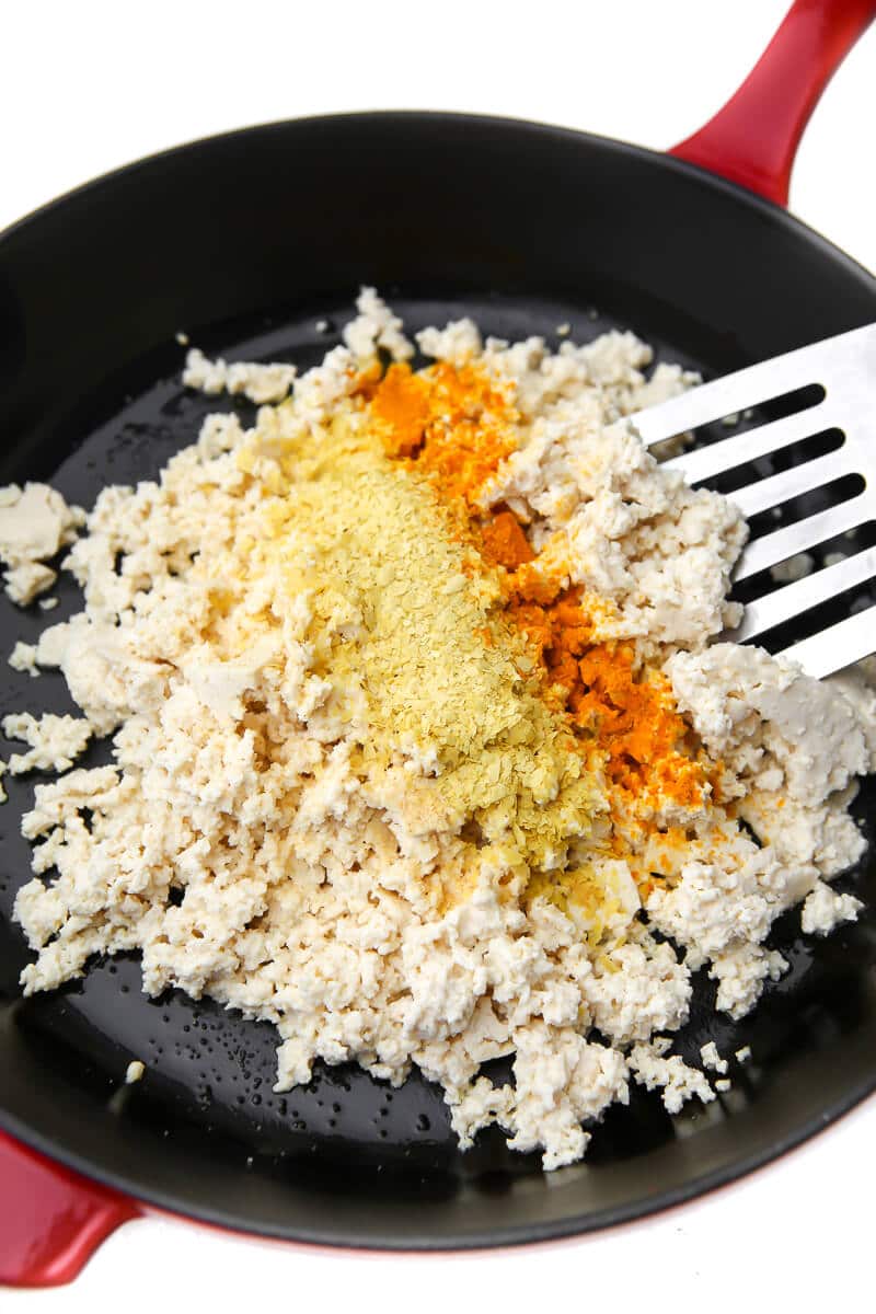 Crumbled tofu, turmeric, salt, garlic power, and nutritional yeast in a skillet before cooking to make a vegan egg substitute.