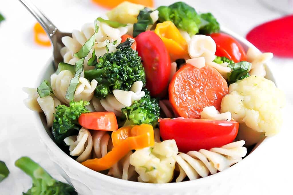 A bowl filled with pasta primavera made with carrots, peppers, broccoli, cauliflower, and tomatoes.
