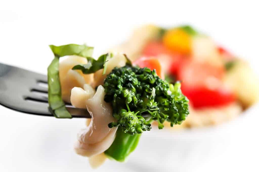 A close up of a fork full of easy pasta primavera with broccoli on it.