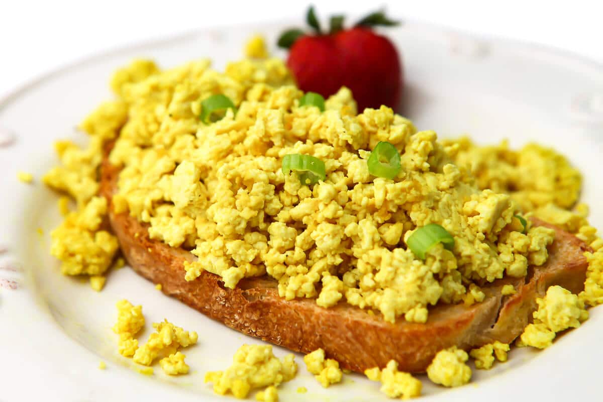 Vegan scrambled eggs on a piece of toast with a strawberry on the side.