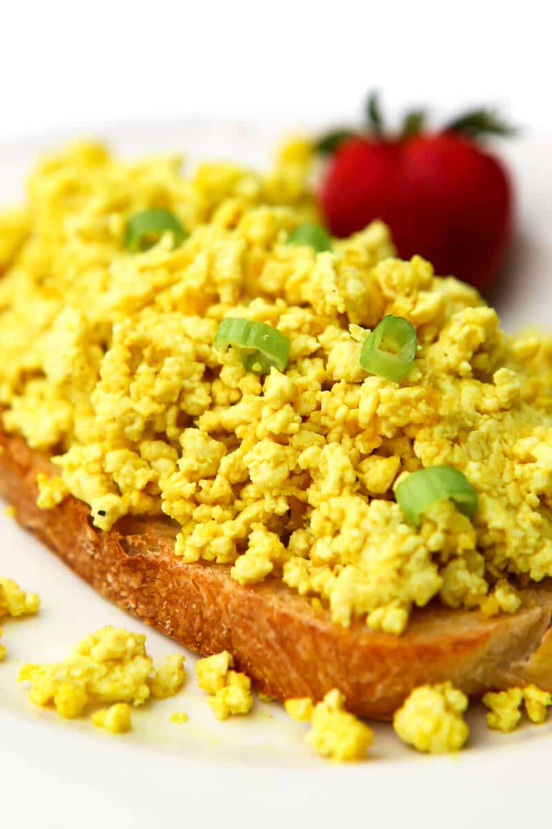 Vegan scrambled eggs on a slice of toast topped with green onion slices.