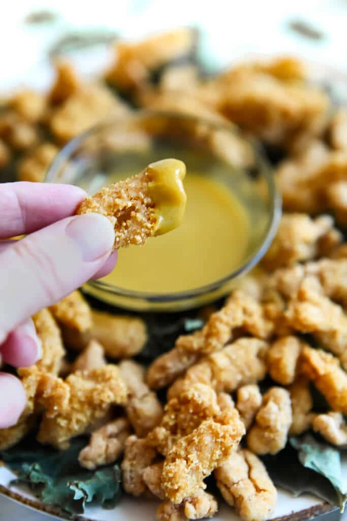 A piece of vegan popcorn chicken dipped into vegan honey mustard sauce.