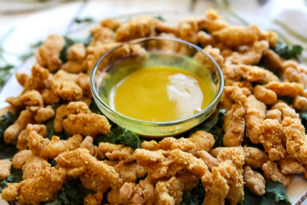 A plate full of vegan fried chicken strips with vegan honey mustard dipping sauce.