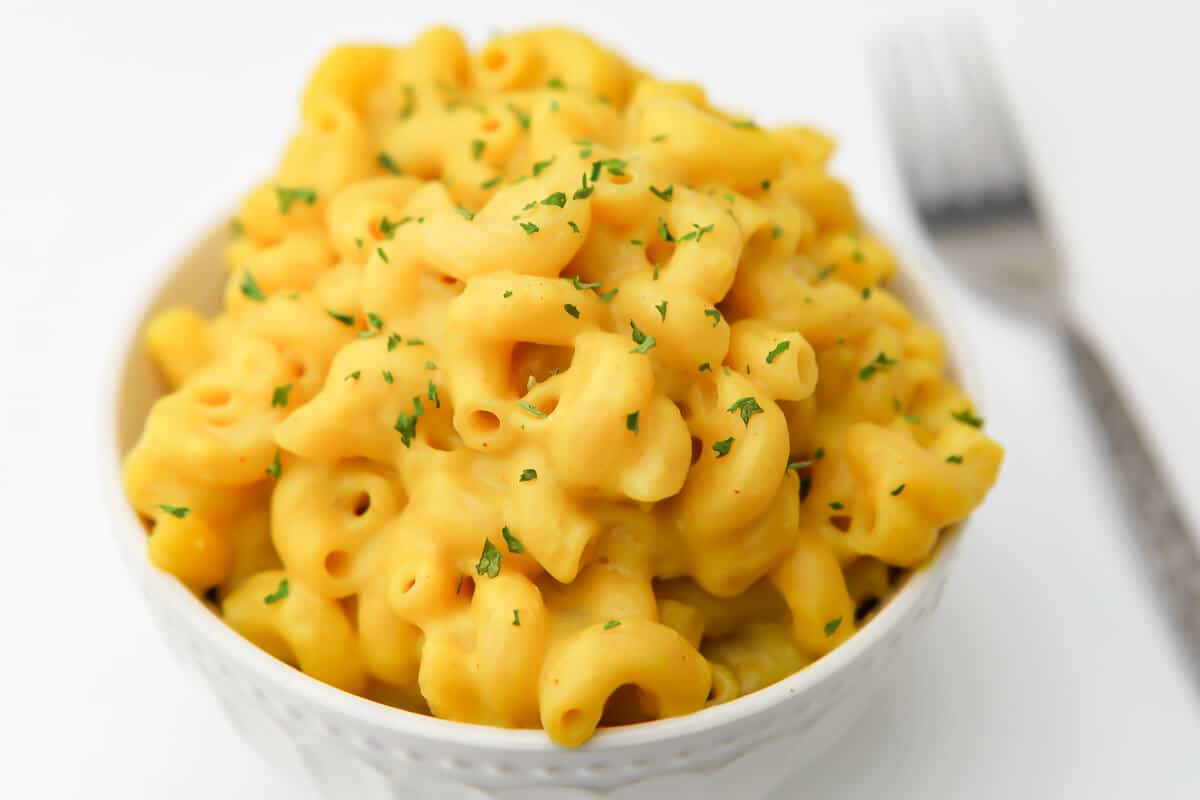 A white bowl filled with mac and cheese and sprinkled with parsley with a fork on the side.