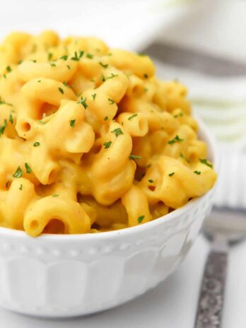 A white bowl filled with vegan mac and cheese with a fork on the side.
