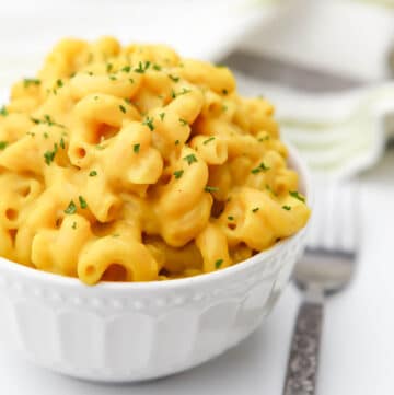 A white bowl filled with vegan mac and cheese with a fork on the side.