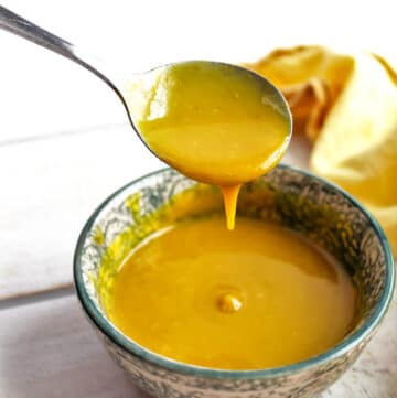 A bowl of vegan honey mustard dipping sauce with a spoonful of honey mustard above it.