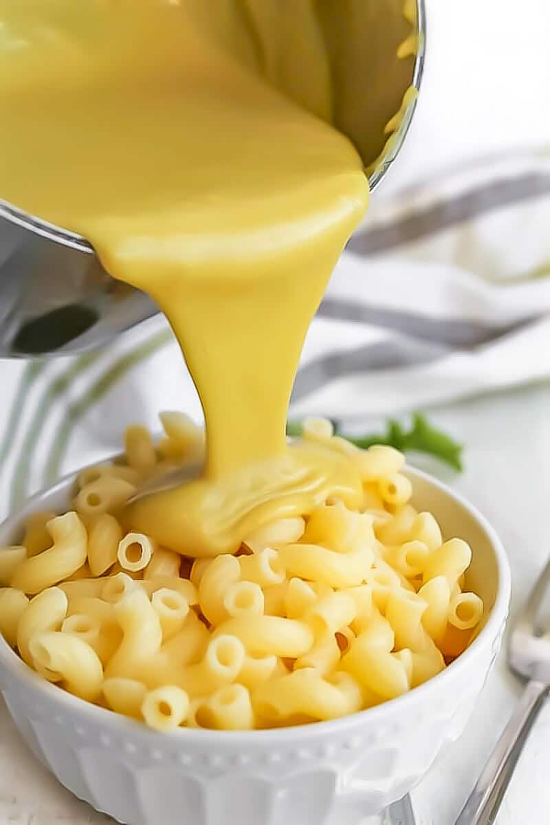 Homemade vegan cheese sauce being poured over a bowl of macaroni.