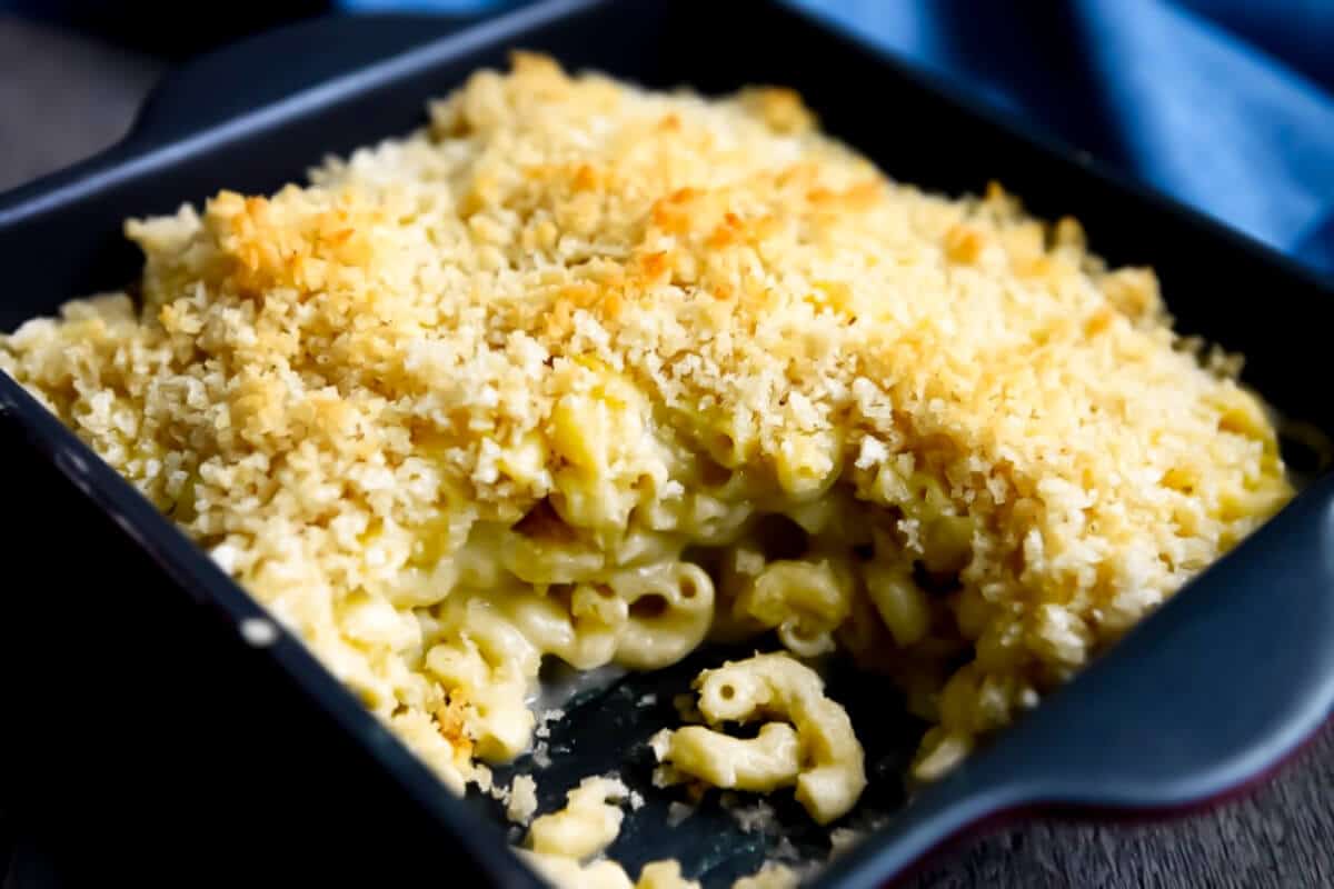 A casserole dish filled with gluten free vegan baked mac and cheese topped with Panko bread crumbs with a scoop taken out..