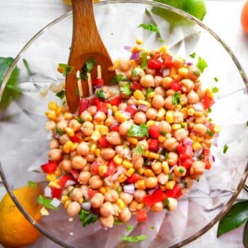 A chickpea citrus salad in a large glass mixing bowl with citrus fruit around it.