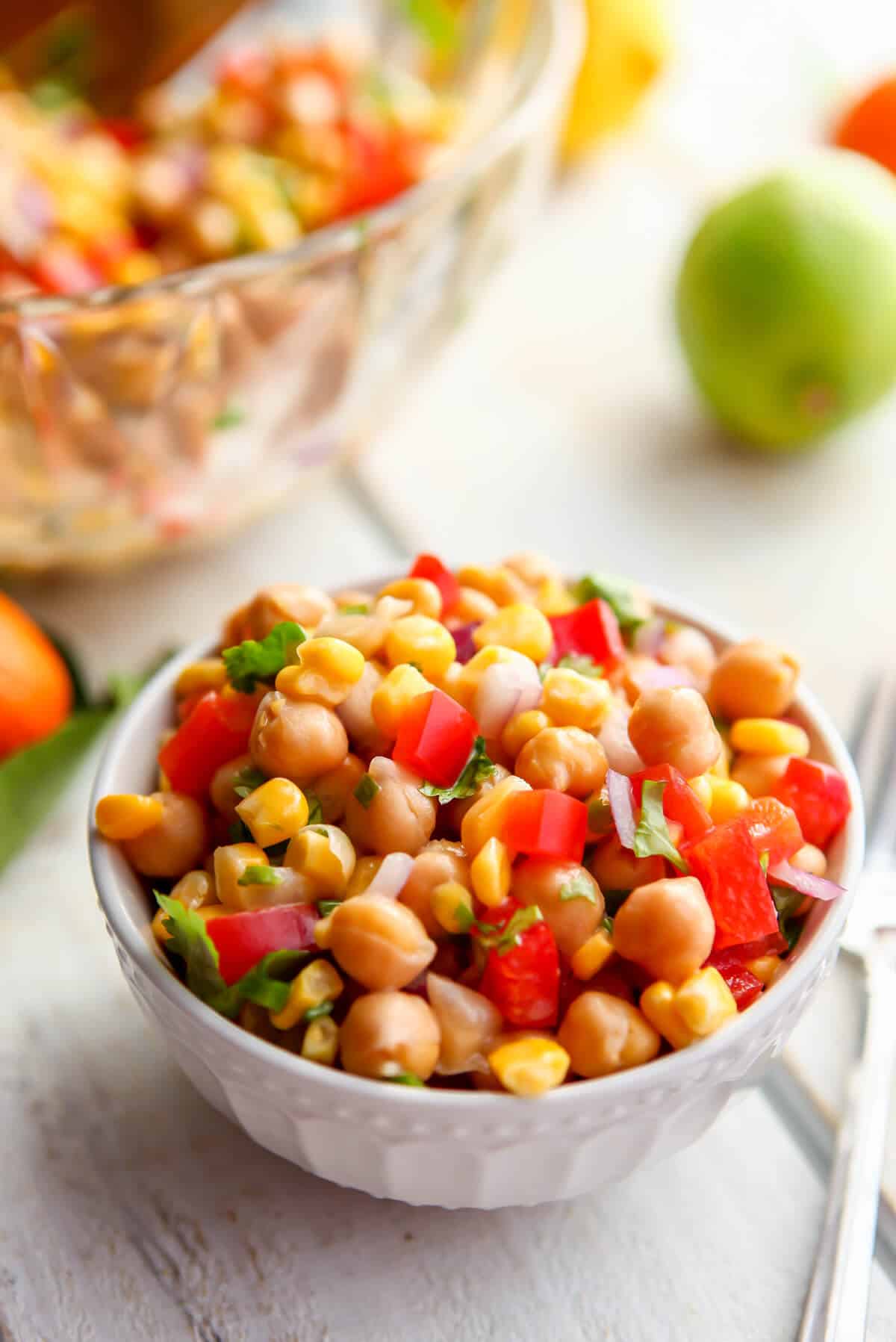 A bowl of chickpea citrus salad next to a lager bowl with lemons, oranges, and limes around it.