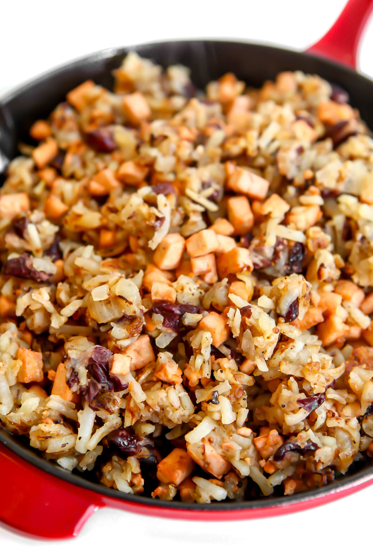 A red iron skilled filled with vegan corned beef hash with a white background.