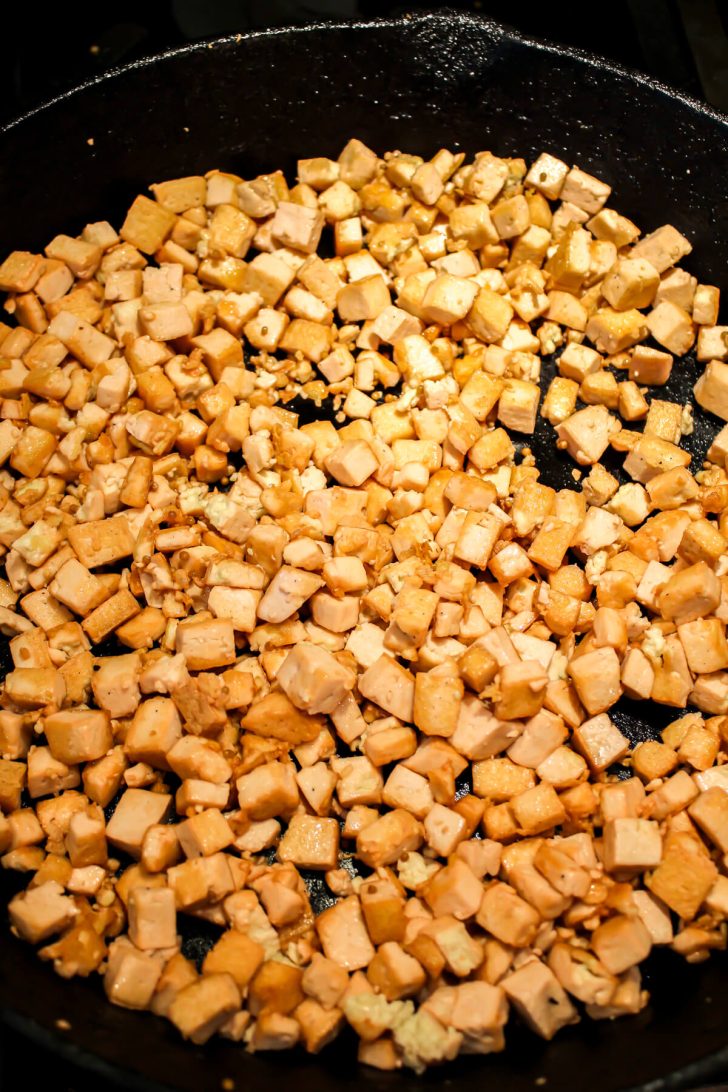 Corned beef flavored tofu cubes frying in an iron skillet.