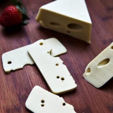 A block of vegan Swiss cheese cut into slices on a wooden cutting board.