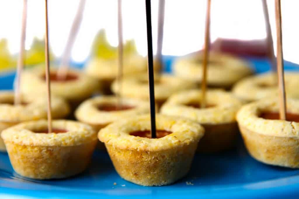 A blue plate full of plant-based corn dog bites with long fancy toothpicks as handles.